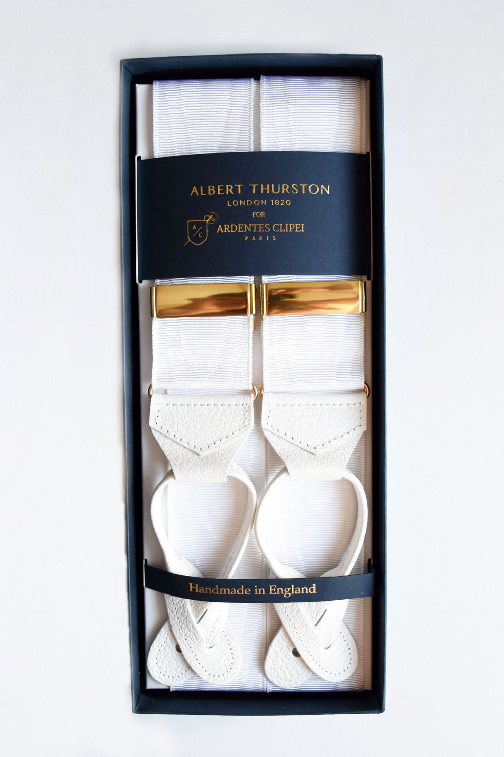White moiré suspenders with gold accents from Albert Thurston, styled with classic adjustable straps for formal wear.