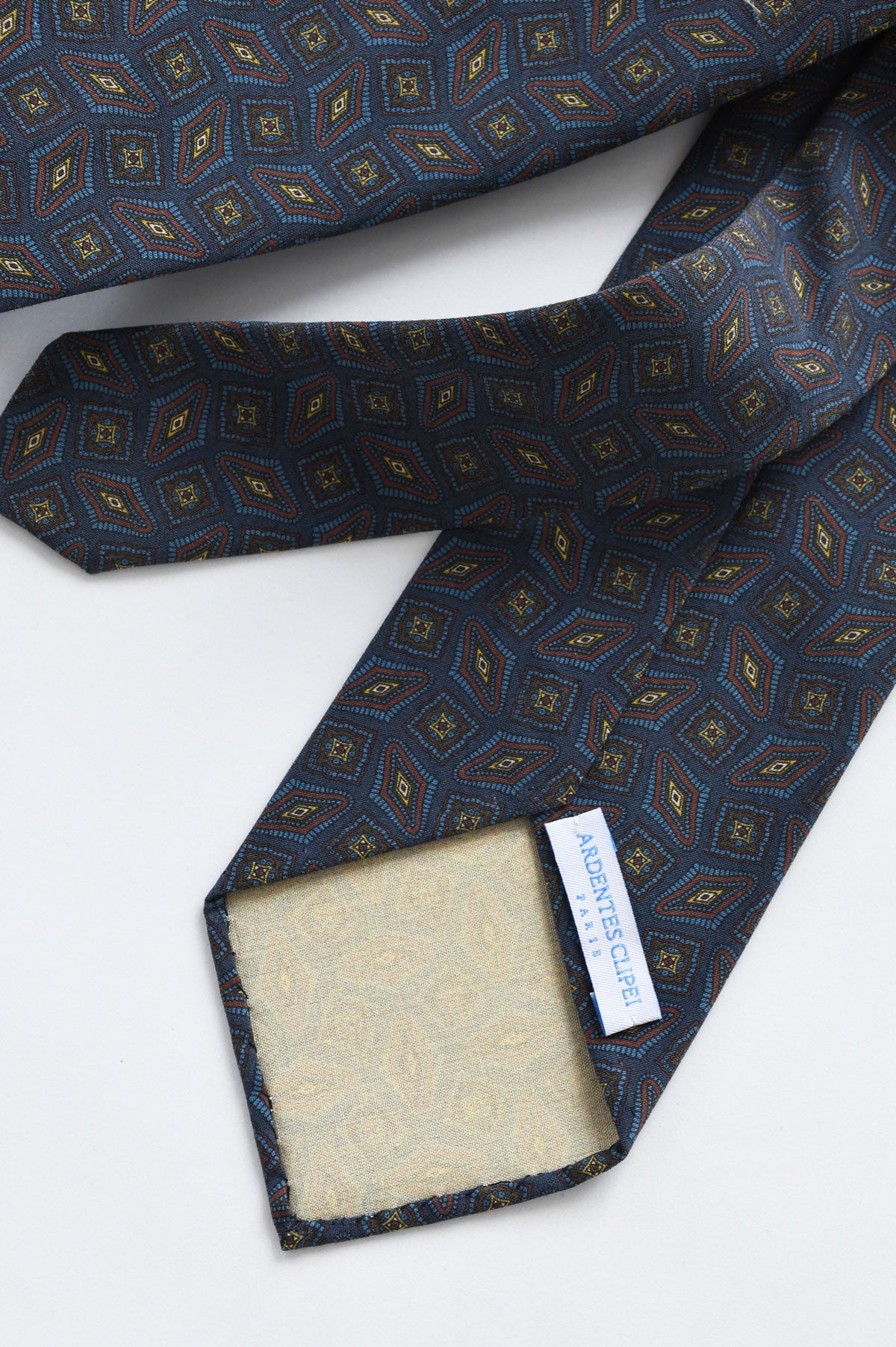 Blue cravate with geometric brown and yellow pattern by Ardentes Clipei, showing the detailed fabric and design.