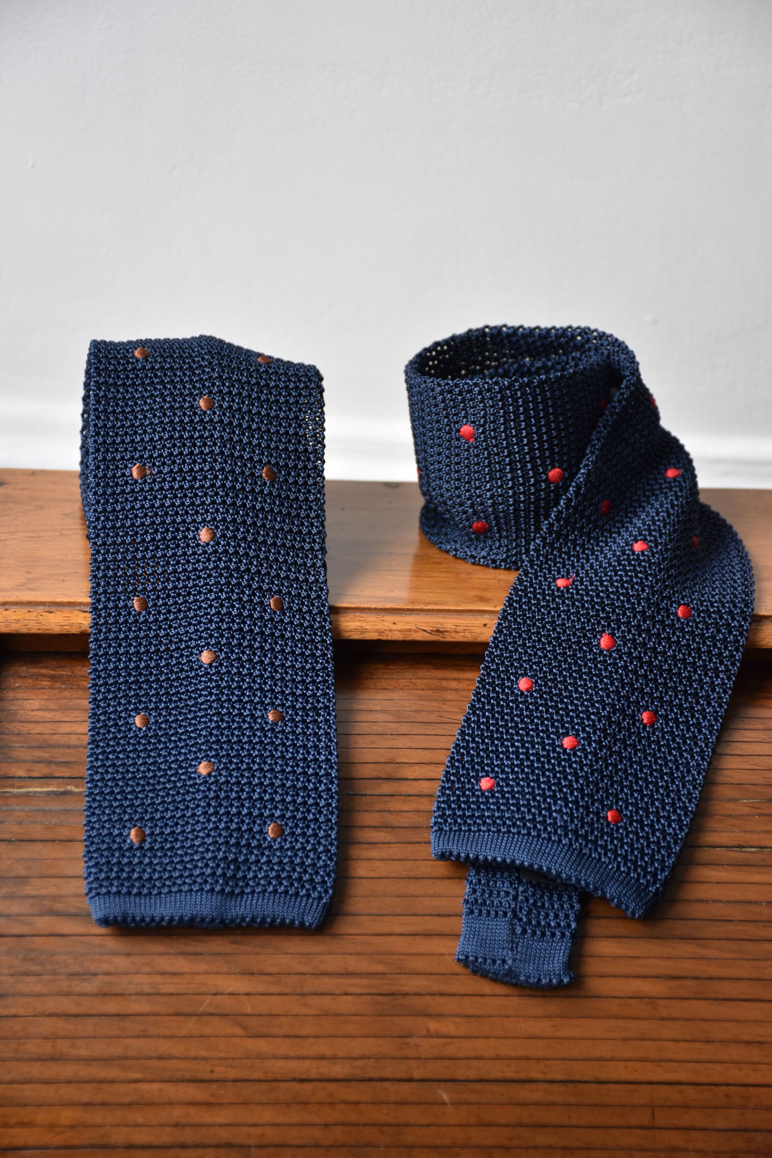 Blue knit tie with brown polka dots from Ardentes Clipei, shown hanging against a neutral background.