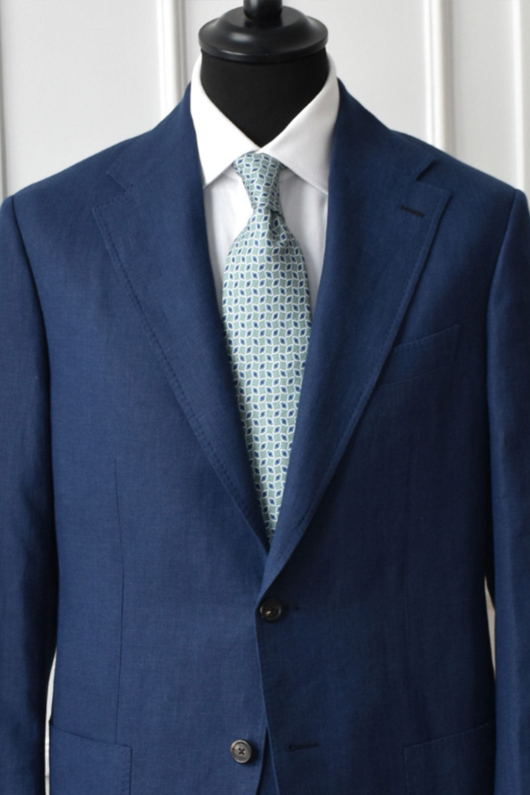 Green water-colored geometric patterned silk and linen tie by Ardentes Clipei, showing intricate design and fabric texture.