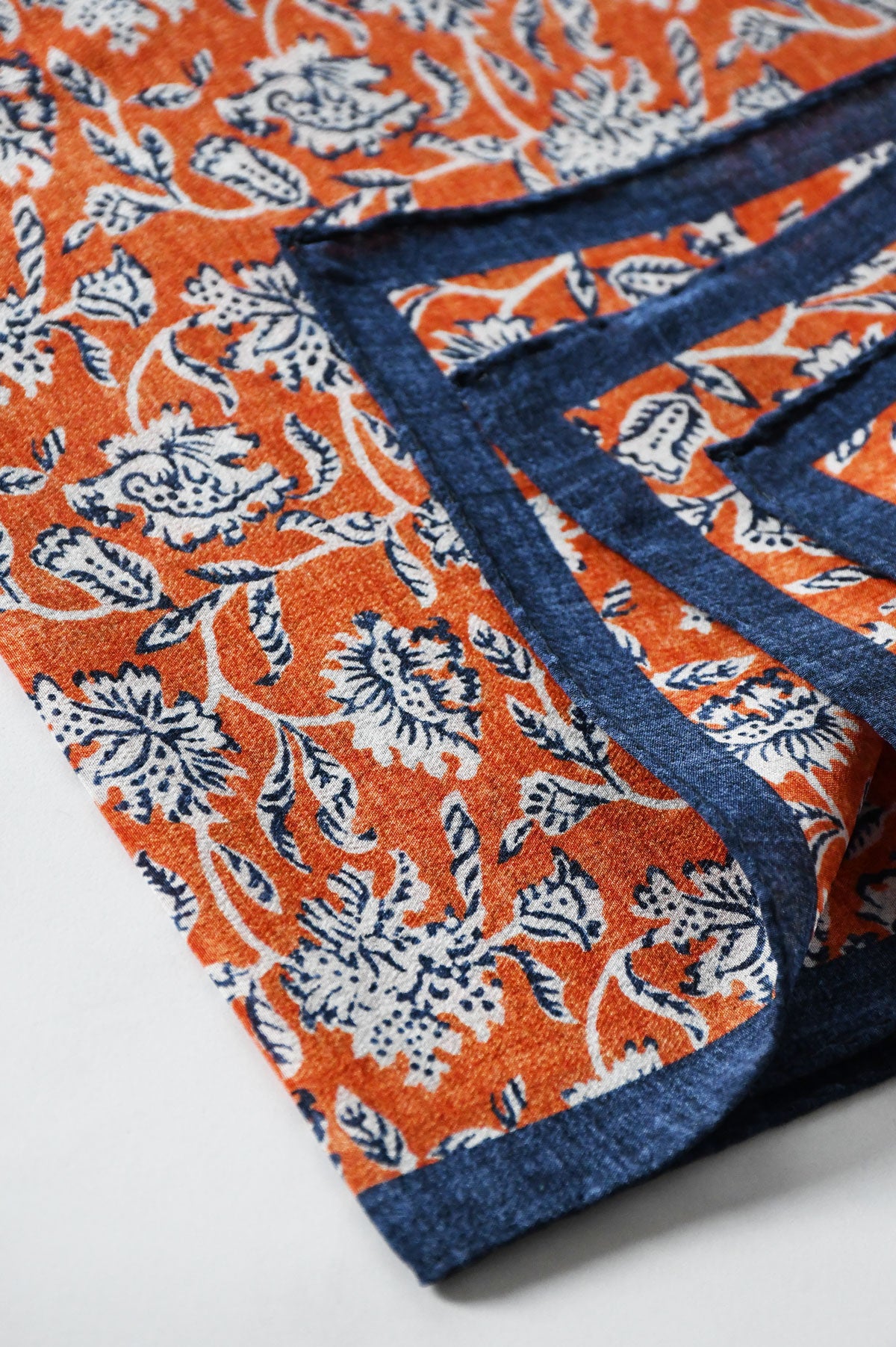 Orange floral motif pochette bag by Ardentes Clipei with vibrant floral patterns and a sleek design.