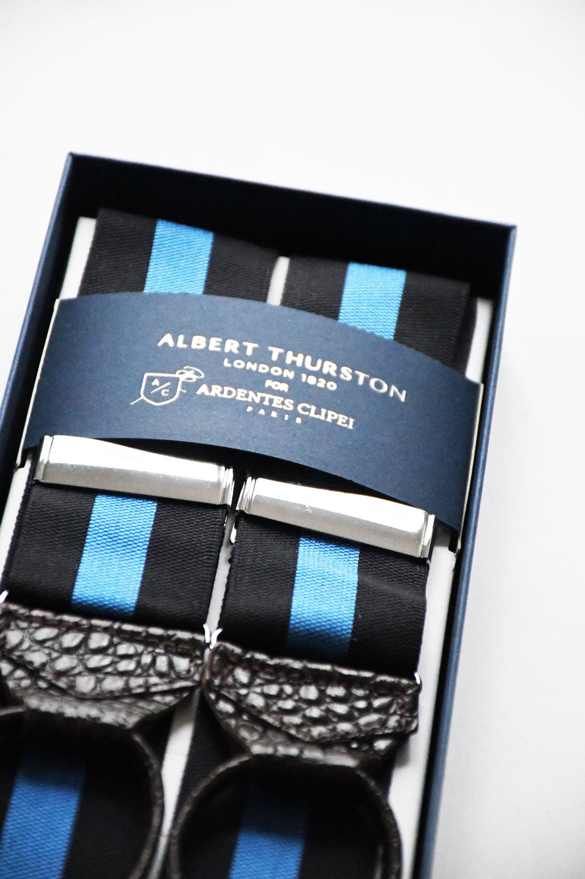 Blue and black striped Albert Thurston suspenders with adjustable straps and metal clasps, worn over a shirt for a classic style.