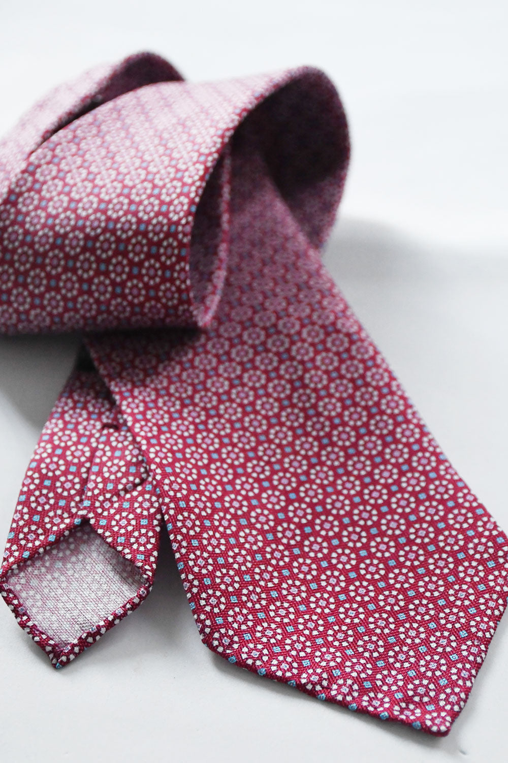 Red raspberry-colored tie with geometric pattern, made of silk and linen, by Ardentes Clipei, displayed flat on a neutral background.