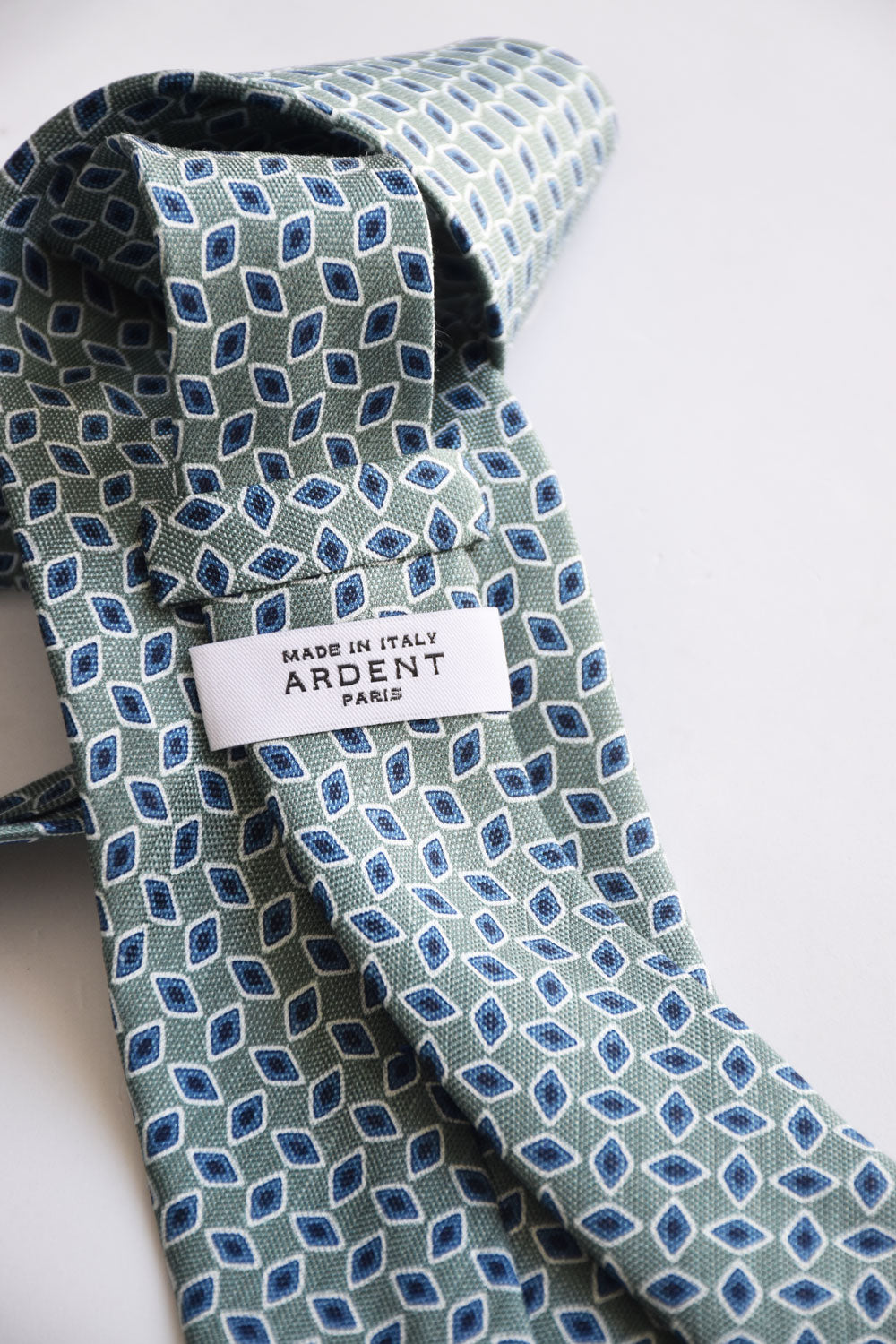 Green water tie with geometric pattern, made of silk and linen, by Ardentes Clipei, displayed flat on a white background.