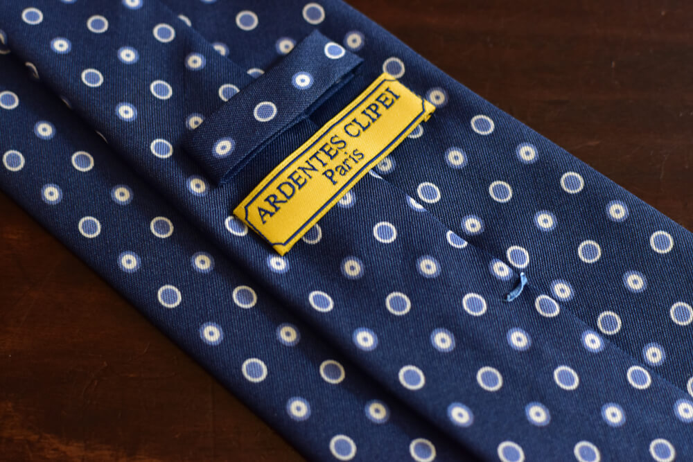 Cravate bleue à pois bleus. Construction 3 plis non doublée et roulotée à la main sur les bords. Motif imprimé à pois et ronds bleus