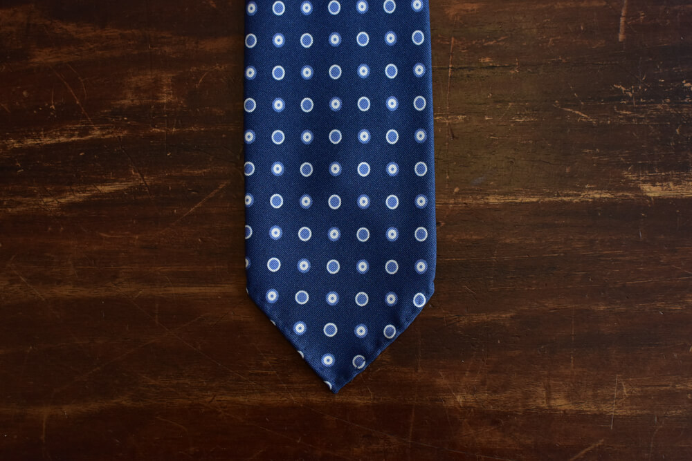 Cravate bleue à pois bleus. Construction 3 plis non doublée et roulotée à la main sur les bords. Motif imprimé à pois et ronds bleus
